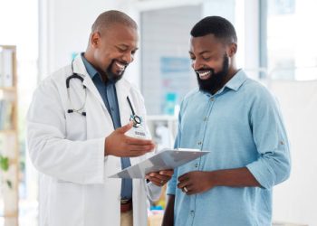 Young patient in a consult with his doctor. African american doctor showing a patient their results on a clipboard. Medical professional talking to his patient in a checkup